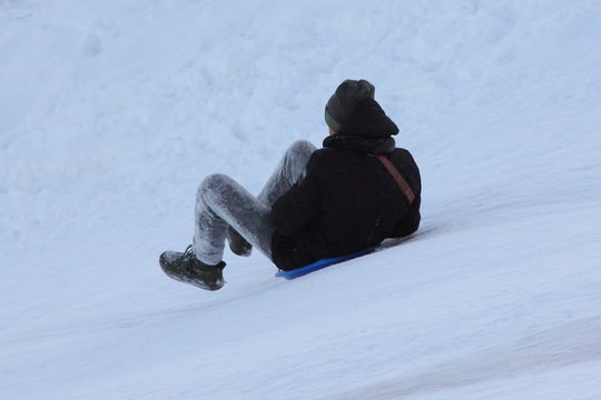 Boy In Jacket And Black Hat Riding From Snowy Mountain On Winter Day - Close Up Rear View