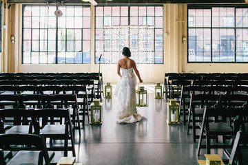 bride walking down aisle holding lantern near empty chairs