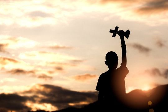 Boy holding christian cross with light sunset background,christian concept.