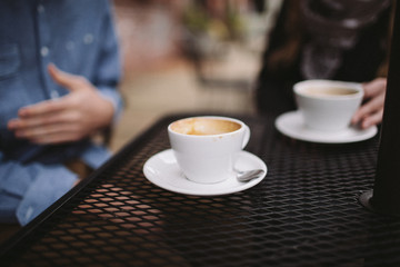 two people sitting near cappucino coffee cups on table outside