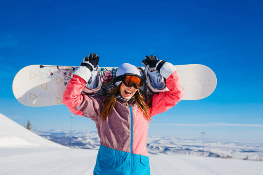 happy cheerful woman in a ski suit and glasses holds a snowboard in her hands in winter. Extreme