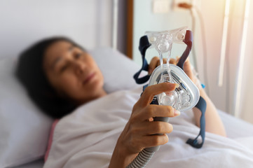 Obstructive sleep apnea therapy..Senior patient woman hands holding Cpap mask  lying  in hospital room,selective focused. - obrazy, fototapety, plakaty