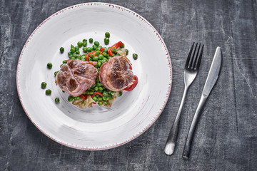 Beef medallions wrapped in bacon, serve with green peas and on a plate on wooden background. Close up