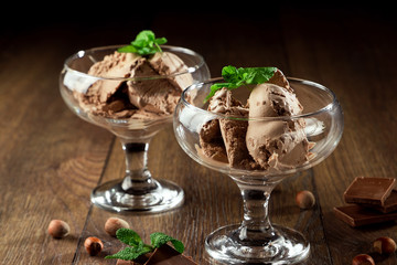 Homemade chocolate ice cream with mint leaves, sprinkled with chocolate in a glass bowl on a wooden table. chocolate pieces, hazelnuts. Selective focus, copy space.