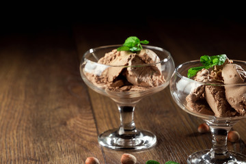 Homemade chocolate ice cream with mint leaves, sprinkled with chocolate in a glass bowl on a wooden table. chocolate pieces, hazelnuts. Selective focus, copy space.