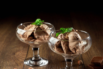 Homemade chocolate ice cream with mint leaves, sprinkled with chocolate in a glass bowl on a wooden table. chocolate pieces, hazelnuts. Selective focus, copy space.