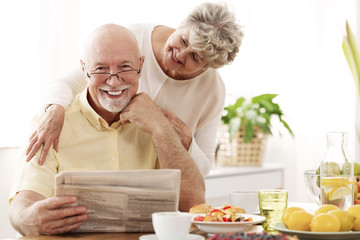 Happy senior couple hugging and smiling. Husband reading a newspaper