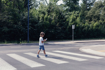 Boy crossing the street while looking at his smartphone