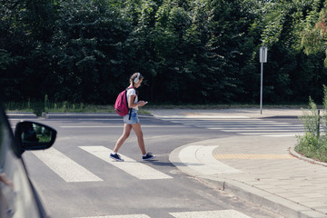 Young girl crossing a street while listening to music and looking at smartphone