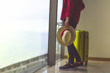 Young woman traveler in casual clothes with a yellow suitcase and a traveler's hat in hands going on vacation.