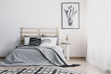 Black and white cactus in pot graphic on the empty white wall of bright bedroom with cozy king size bed , real photo with copy space