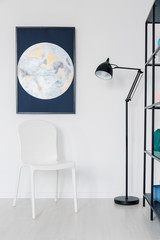 Naklejka premium Vertical view of white chair in white interior with moon graphic on the wall and metal lamp, real photo