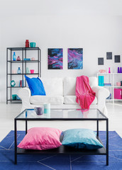 Galaxy graphics on the wall of colorful living room with white couch with blue pillow and pink blanket, real photo with copy space on the empty wall
