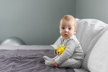 Sitting baby boy on grey carpet with yellow ball toy. Motherhood and new life concept