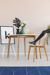 Blue carpet and model's leg in dining room interior with chair at wooden table with leaf. Real photo