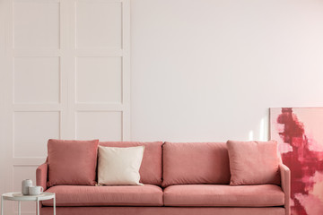 Burgundy and pastel pink abstract painting in white living room interior with velvet sofa with...