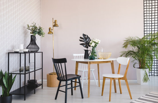 White And Black Chair At Wooden Table With Plant In Dining Room Interior With Gold Lamp. Real Photo