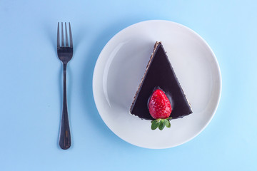 A slice of sweet strawberry cake with dripping chocolate glaze in a white plate and fork on a blue background. Sweet dessert. Top view