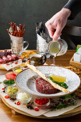 Male hand pours olive oil on fresh delicious beef tartare. Minced meat with ingredients for tartar