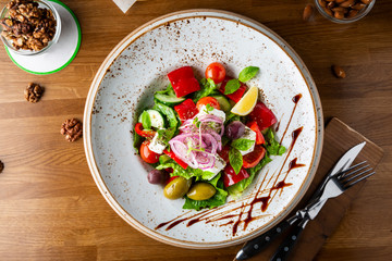 Greek salad with feta cheese, olives and herbs, served in a white plate on a table in a restaurant.