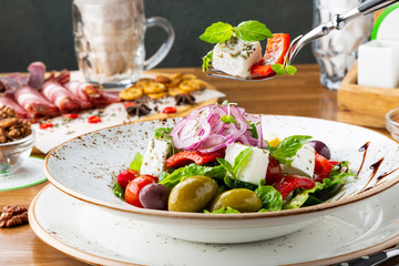 Greek salad with feta cheese, olives and herbs, served in a white plate on a table in a restaurant.