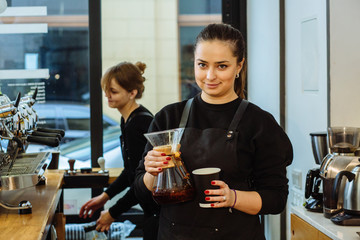 Young female barista in black uniform preparing coffee drink. Skillful staff and team work concept.