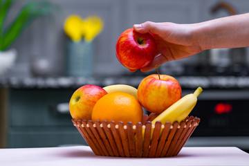 Fresh fruits - orange, banana, apples in a wooden bowl in a kitchen at home.