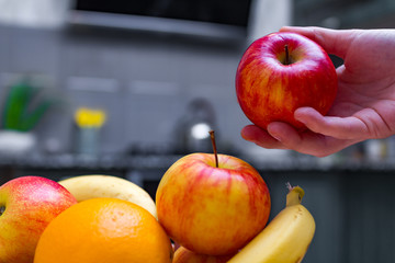 Fresh fruits - orange, banana, apples in a wooden bowl in a kitchen at home.