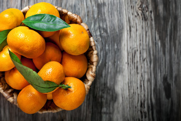 Tangerines with leaves in basket on rustic wooden background.