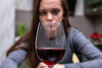 Depressed, divorced crying woman sitting alone in kitchen at home and drinking a glass of red wine because of problems at work and troubles in relationships. Social and life problems