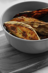 Baked potato and rosemary wedges in a grey bowl on a wooden chopping board with selective colour