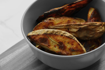 Baked potato and rosemary wedges in a grey bowl on a wooden chopping board with selective colour