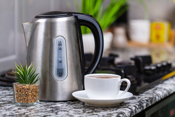 Brewed tea in a white cup and an electric kettle on the table in the kitchen at home. Time for breakfast