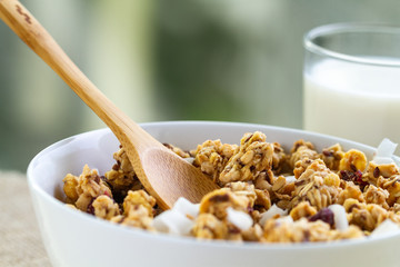 Dry breakfast cereals. Crunchy honey granola bowl with flax seeds, cranberries, coconut and a glass of milk close up. Healthy, clean and fiber food