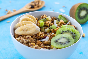 Dry breakfast cereals. Crunchy honey muesli bowl with slices of fresh banana and kiwi on a blue background. Raw diet and fiber food. Breakfast time