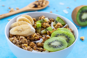 Dry breakfast cereals. Crunchy honey muesli bowl with slices of fresh banana and kiwi on a blue background. Raw diet and fiber food. Breakfast time