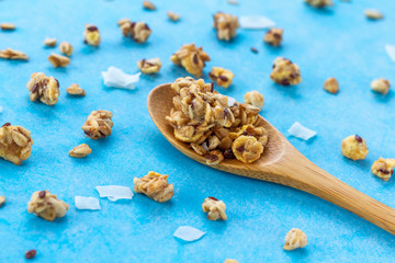 Dry breakfast cereals. Crunchy honey granola with flax seeds, cranberries and coconut in a wooden spoon on a blue background. Healthy and fiber food