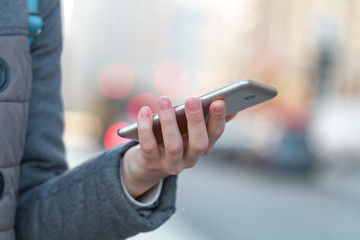 Woman is holding a mobile phone on the background of the city. Mobile communications and applications. Dependence on the phone and social networks