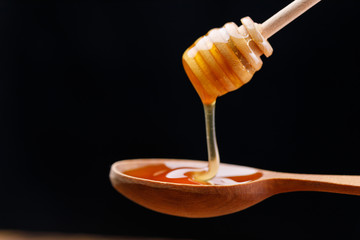 A wooden spoon and honey pouring from it. Close-up.