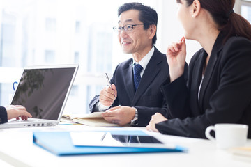 窓際の明るいデスクで笑顔で話し合いを行う会社員