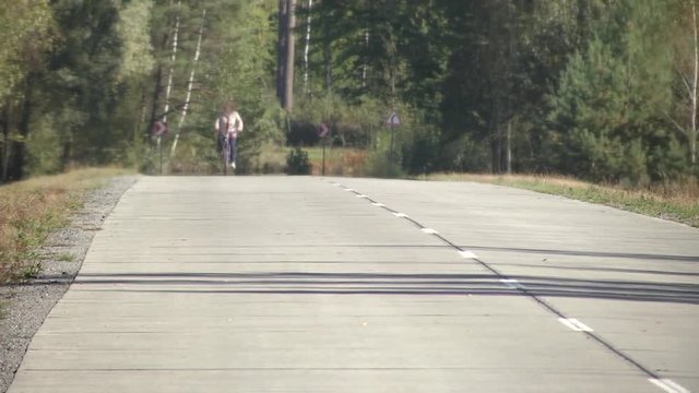 A forest road prepared for vehicular traffic. Concrete road in the forest. On the concrete road new road markings. Cyclist rides through the forest road.