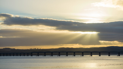 Fototapeta premium Old railroad bridge at sunset/sunrise, rays of sunlight leading way through clouds