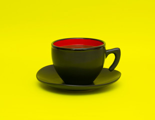 Black cup with hot tea on the yellow background