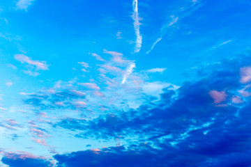 Fototapeta na wymiar Pattern of blue, pink and white clouds, airplane trails on blue sky