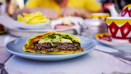 in a restaurant on the dinner table in a blue plate lies a burger in pita bread with beef cutlet, cheese and vegetables, in the background a person without focus