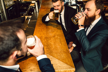 Young businessman in suit drink bear in bar. They sit in front of each other.