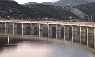 Late afternoon bridge mirroring on water. Lake Polyfytos at Haliacmon river, central Greece