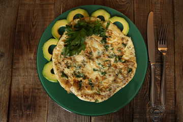 omelette with fresh parsley and avocado in a green plate on a wooden oak background
