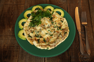 omelette with fresh parsley and avocado in a green plate on a wooden rustic background
