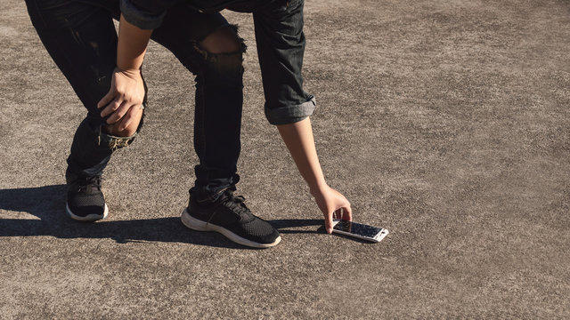 Young man picking broken and cracked screen smartphon from floor after dropped with copy space. Concept of broken or accident mobile phone, repair, warranty and technology